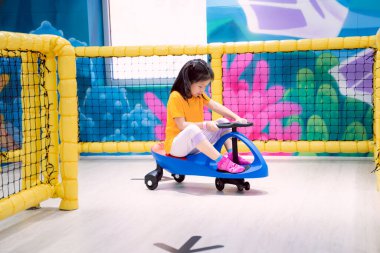 A child is having fun playing with a blue toy car, a cute Asian girl plays in an indoor playground. Children aged 7 years. clipart