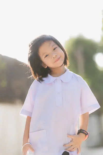 stock image Portrait of a smiling Asian child in the park during summer. Kid sweet smiling and good mood. Schoolgirl wearing school uniform. Vertical images. Back to school.