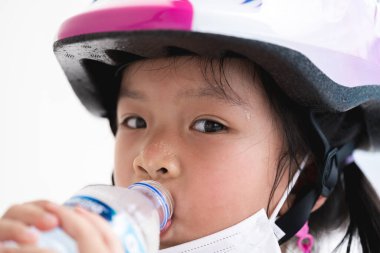 Sıcak bir günde, yaz mevsiminde, bir şişeden su içen, egzersiz yaptıktan sonra susayan, bisiklet süren, kask takan tatlı bir kızın yakın çekimi. Genç Asyalı çocuklar çok terler..