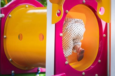 Dışarıdaki bir oyun parkında oyuncak tünelinde sürünen kız çocuğunun arka görüntüsü. Çocuk mutlu mesut oynuyor ve eğleniyor. Yaz ya da bahar aylarında. Koşmak ve egzersiz yapmak. Çocukluk macerası gezisi.