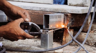 Çeliği kaynak yapan bir teknisyenin yakın çekimi, işten küçük kıvılcımlar. Bir kaynakçı fabrikada çalışır, ateş ve aletlerle metal şekillendirir..