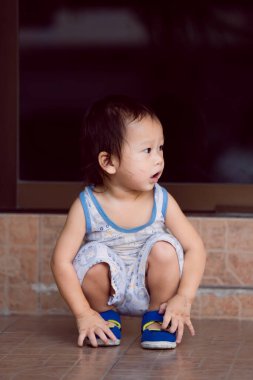 1-2 yaşındaki Asyalı küçük çocuk yere çömelmiş, kirli suratlı çocuk sihirli renkli kalemle oynadıktan sonra oturuyor ve bir şeye bakıyor. Akşamları. Pozitif ruh hali. Dikey.