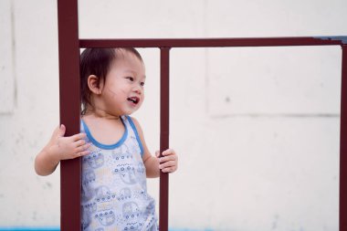 Asyalı bir çocuk, 1-2 yaşlarında, bahçesinde demir bir çite mutlu bir şekilde tırmanıyor, tatlı tatlı gülümsüyor, yüzü yaz ya da bahar aylarında yaramazlık izleri taşıyor. Boşluğu Kopyala.