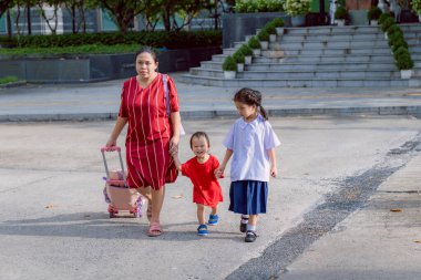 Mom sending her daughter to school, Mom holding her son's hand, Sibling holding hands walking, Back to school for the first semester, girl wearing school uniform with white shirt and navy blue skirt. clipart