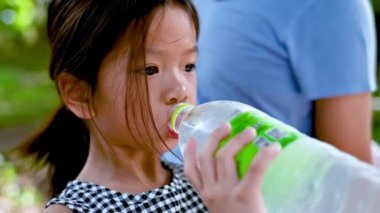 Asyalı kız plastik şişeden soğuk su içiyor. Çocuk sıcak hava nedeniyle susadı. Yazın..