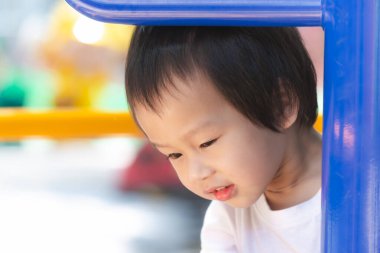 Asyalı genç çocuk meraklı bir şekilde bakıyor, oyun bahçesinin altından dışarı bakıyor, masum bir merak ve keşfin resmi. Yakından Meraklı çocuk.