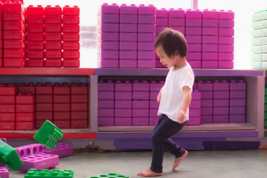 Asyalı küçük çocuk mutlu bir şekilde oyuncak bloklarda oynuyor ve çocuğun inşa ettiği oyuncakları tekmeliyor. 2 yaşında bir çocuk evin içinde oyuncaklarla oynuyor..