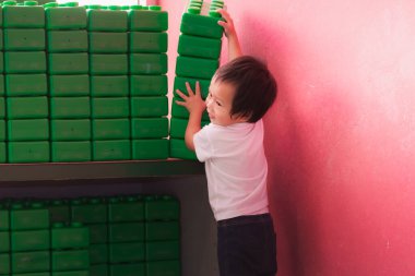 Küçük Asyalı çocuk yeşil oyuncak bloklarıyla oynuyor, oyuncakları raftan kaldıran çocuk, mutlu 2 yaşında bir çocuk..