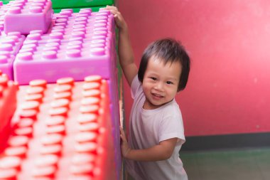 Genç bir çocuk, kapalı bir oyun alanında renkli plastik oyuncak yapı taşlarıyla oynarken eğleniyor. 2 yaşında tatlı, gülümseyen bir çocuk. Tatlı gülümseme.