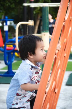 2 yaşındaki Asyalı bir çocuk tırmanırken eğleniyor. Küçük çocuk oyuncağın üzerinde eğleniyor. Güneşli bir günde oyun parkında duvara tırmanıyor..
