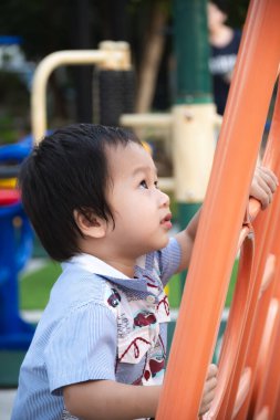 2 yaşındaki Asyalı bir çocuğun, yaz ya da baharda açık hava çocuk parkındaki turuncu tırmanma parkında brüt ve iyi motor becerileri öğrenip geliştirdiği dikey fotoğrafı..