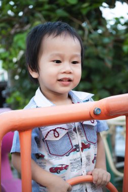 Çocuk bahçesinde oyuncaklara tırmanırken eğlenen gülümseyen çocuğun yakın plan portresi, 2 yaşında hevesli Asyalı bir çocuk, kas gelişimi.