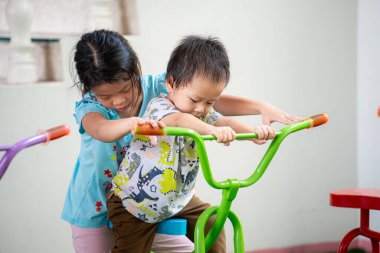 Kız kardeşi küçük erkek kardeşine oyun parkında bisiklet sürmeyi öğretiyor. Kardeşlerin birlikte eğlendiği mutlu an kavramı..