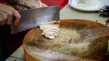 Ahşap kesme tahtasında tavuk kesmek için bıçak kullanan bir aşçının resmi..