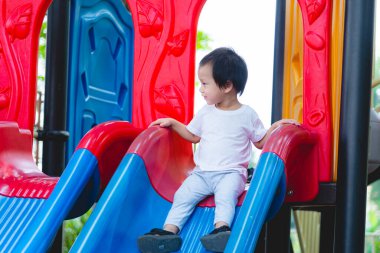 Oyun parkında küçük bir çocuk. 2 yaşında tatlı bir çocuk parktaki çocuk parkında büyük bir kaydırağın üstünde tırmanıp kayıyor..