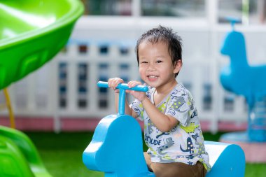 Küçük çocuk dışarıda oyun sahasında eğleniyor. Sıcak bir yaz ya da bahar günü, çocuğun yüzü ter içinde, saçı terden sırılsıklam olur. 2-3 yaşlarında Asyalı bir çocuk..
