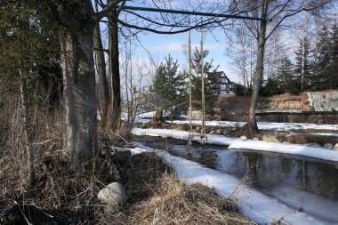 Güneşli bir günde kar ve buzla kaplı kış nehri. Mavi gökyüzü, beyaz ışık bulutları, tepe üzerindeki büyük kayalık nehir kıyısı..