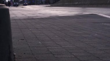 Erkek ayakları kot pantolon ve siyah ayakkabılarla kentteki yaya yolunda yürüyen arabalar ve tramvaylar.