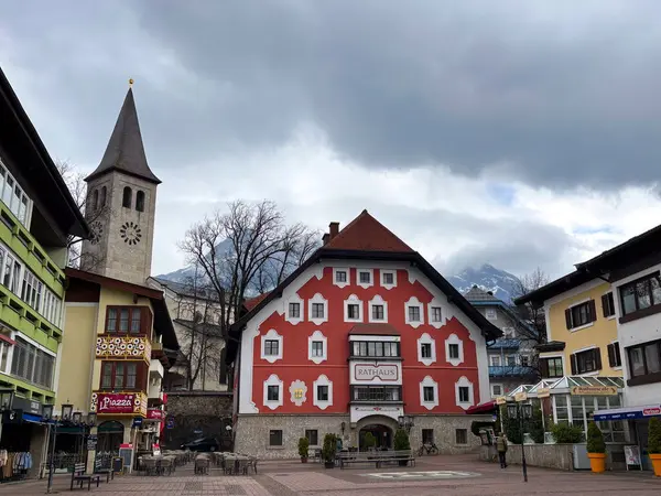 SAALFELDEN, AUSTRIA - 26 Mart 2025 - Saalfelden belediye binasında yağmurlu manzara. Zell am Bölgesi Avusturya 'da. Kilise, ana meydan, etrafta insan yok ve su var, arka planda dağlar.