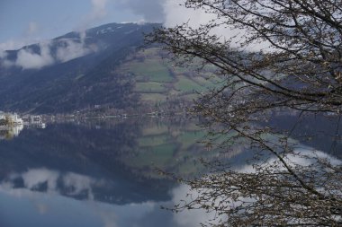 Avusturya Alpleri 'nde yer alan Zell am See' nin bulutlu hava günlerinde bankları kapatın. Arkaplanda dağlar ve şehir, saf suyun üzerinde yansıyor.