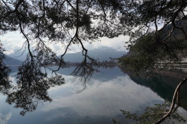 Avusturya Alpleri 'nde yer alan Zell am See' nin bulutlu hava günlerinde bankları kapatın. Arkaplanda dağlar ve şehir, saf suyun üzerinde yansıyor.