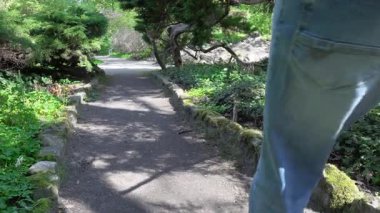 Beyaz tişörtlü, kot pantolonlu, siyah şapkalı bir adam güneşli bir günde kumlu yolda yürüyor.