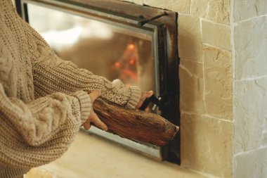 Çiftlik evindeki kır evindeki şömineye odun koyan kadın. Kışın odun sobasıyla ısıtma evi. Gaz ve elektriğe alternatif olarak şömine ısıtma