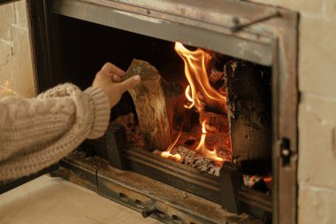 Kışın odun sobasıyla ısıtma evi. Çiftlik evindeki kır evindeki şömineye odun atan kadın. Gaz ve elektriğe alternatif olarak şömine ısıtma