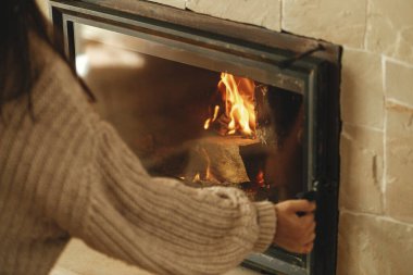 Kışın odun sobasıyla ısıtma evi. Çiftlik evindeki köy odasındaki şömineye odun koyan kadın. Gaz ve elektriğe alternatif olarak şömine ısıtma