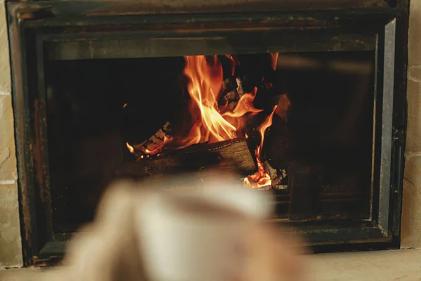 用烧木柴的火炉加热房子 烧着的壁炉靠得很近 用一杯热茶 秋天的烈酒模糊了双手 舒适的乡村壁炉中的放松和热身 — 图库照片