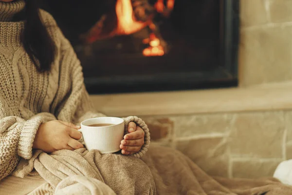 手拿着舒适的毛衣 拿着一杯热茶 背靠着燃烧的壁炉 秋天的湿气 在乡村壁炉放松和热身 用烧木头的火炉取暖的房子 — 图库照片