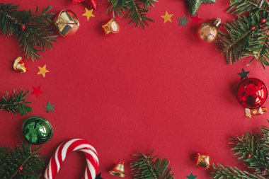 Modern noel yatağı. Şık Noel süsleri, köknar dalları ve kırmızı arka planda konfeti çerçevesi. Mevsimlik tebrik kartı şablonu, metin için boşluk. Mutlu Noeller ve mutlu tatiller!