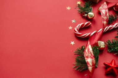 Mutlu Noeller! Modern Noel 'de hala hayat var. Şık Noel şekerlemeleri, takılar, köknar dalları, kırmızı arka planda konfeti. Mevsimlik tebrik kartı, mesaj için yer. Kış tatili afişi