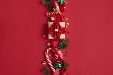 Modern noel yatağı. Şık bir Noel hediyesi, takılar, köknar dalları, baston şekerler, kırmızı arka planda konfeti. Mevsimlik tebrik kartı, mesaj için yer. Mutlu Noeller! Kış tatili afişi