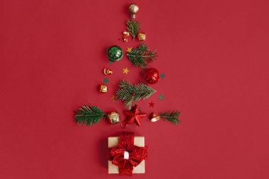 Mutlu Noeller! Köknar dallarından, takılardan, altın konfetilerden ve kırmızı arka planda hediyelerden oluşan şık bir Noel ağacı. Yaratıcı bir fikir. Kış tatili, modern afiş