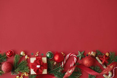 Modern noel yatağı. Şık bir Noel hediyesi, takılar, köknar dalları, konfeti ve kırmızı arka planda şeker kamışı. Mutlu Noeller! Mevsimlik tebrik kartı şablonu, metin için boşluk. Kış tatili