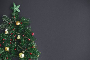 Noel ağacı, kış tatili konsepti. Köknar dallarından, kırmızı böğürtlenlerden ve siyah arka planda altın takılardan yapılmış şık bir Noel ağacı. Yaratıcı bir fikir. Modern bayrak