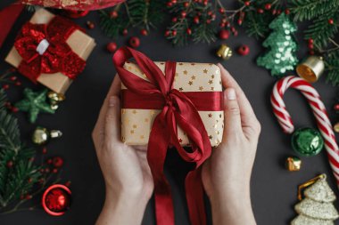 Elleri şık bir Noel hediyesi, siyah arka planda kırmızı kurdele, modern şenlik dekorasyonları, üst manzara. Kış tatili afişi. Mutlu Noeller ve mutlu tatiller!