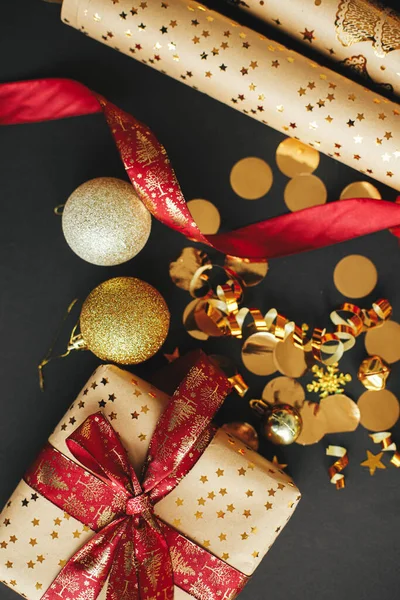 現代のクリスマスプレゼントフラットレイアウト 赤いリボン 包装紙 金色のコンフェッティと黒の背景に赤ちゃんとスタイリッシュなクリスマスプレゼント メリークリスマスとハッピーホリデー — ストック写真