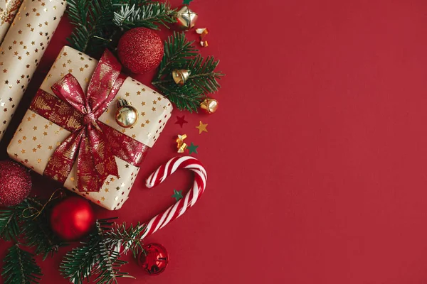 現代のクリスマスのフラットレイアウト スタイリッシュなクリスマスプレゼント 包装紙 モミの枝 赤い背景にキャンディ杖とベーブルの組成物 コピースペース メリークリスマスとハッピーホリデー — ストック写真
