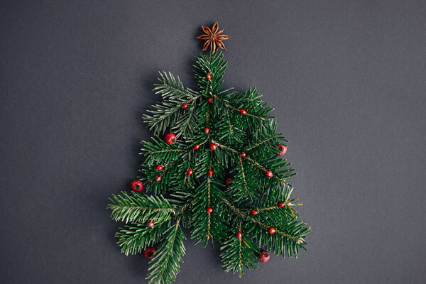 Stylish christmas tree made of fir branches, red berries and anise star on black background, creative idea. Winter holidays, seasons greeting card. Merry Christmas! Modern festive flat lay