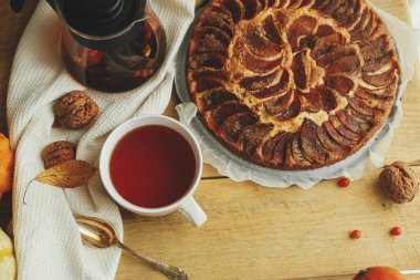 Atmosferik sonbahar natürmort. Tarçınlı, mumlu, sonbahar yapraklı ve fındıklı taze pişmiş elmalı turtayla sade bir masada, şık bir fincanda ılık çay. Hygge evde. en üstteki görünüm