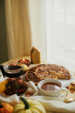 Atmosferik sonbahar natürmort. Tarçınlı, mumlu, sonbahar yapraklı, balkabaklı ve fındıklı taze elmalı turta ile sade ahşap masada, şık bir fincanda ılık çay. Hygge evde, rahat bir an.