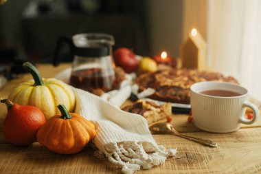Atmosferik sonbahar natürmort. Balkabakları, tarçınlı, mumlu, sonbahar yapraklı ve fındıklı taze elmalı turta ile ahşap masa üzerinde şık bir fincanda ılık çay. Hygge evde, rahat bir an.