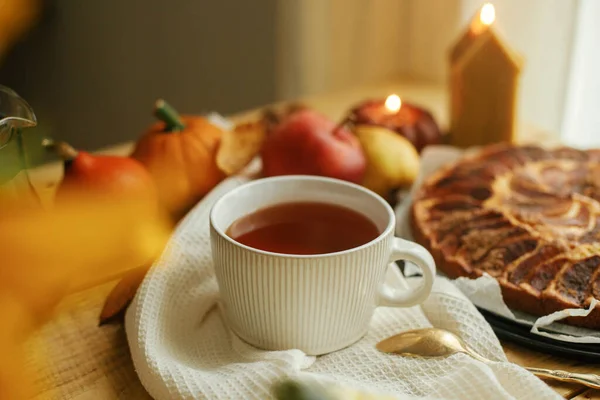 stock image Atmospheric autumn still life. Warm tea in stylish cup on rustic wooden table with freshly baked apple pie with cinnamon, candle, autumn leaves and nuts. Hygge home, cozy moment