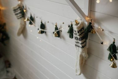 Stylish christmas stocking, garland and lights in festive decorated boho room. Rustic holiday handmade decoration, scandinavian style. Woolen sock and garland in home