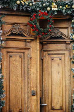 Şık Noel çelenkleri ve binadaki eski ahşap kapılara köknar dalları. Şehir caddesinde modern noel dekorasyonu. Avrupa 'da kış tatili. Mutlu Noeller.