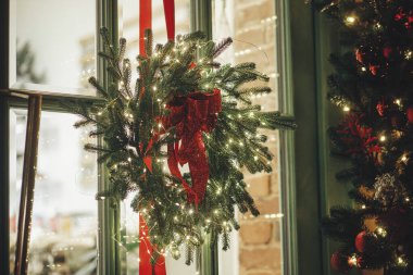 Işıklı bir Noel çelengi ve akşam kapısında yay. Şehir caddesinde modern noel dekorasyonu. Avrupa 'da atmosferik kış tatili. Mutlu Noeller ve mutlu tatiller!