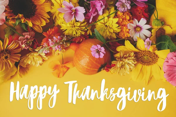 Happy Thanksgiving greeting card. Happy Thanksgiving text and colorful autumn flowers, pumpkins, squashes flat lay on yellow background. Season\'s greetings, handwritten lettering