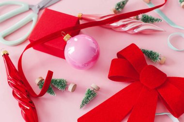 Kış tatili konsepti. Şık kırmızı fiyonk, takılar, küçük yeşil ağaçlar, kurdeleler ve pembe arka planda hediye. Yaratıcı pembe noel kompozisyonu. Mutlu Noeller ve mutlu tatiller!